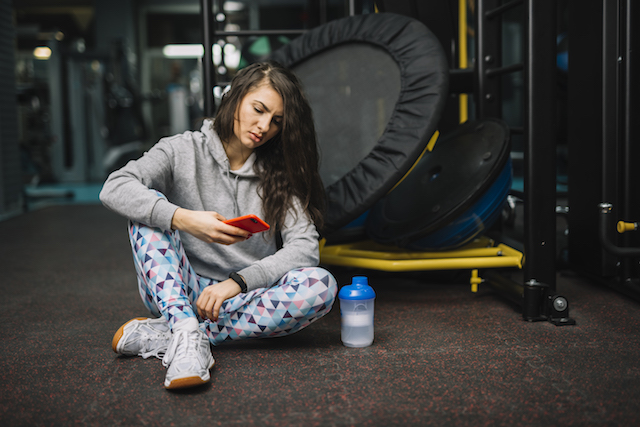 woman looking unhappy looking at her phone at the gym.