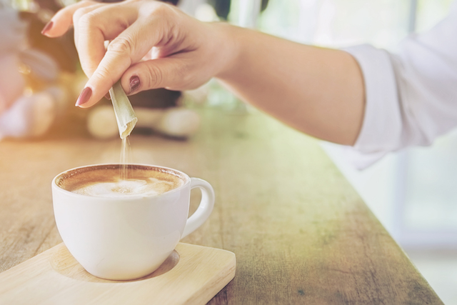 woman pouring a packet of sugar into her coffee.