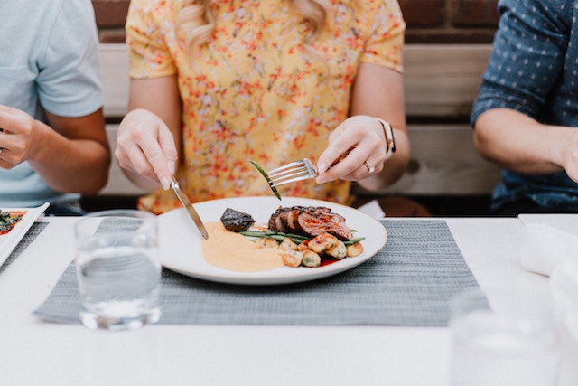 woman eating a plate of food that has protein and vegetables.