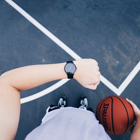 person looking down at watch while holding a basketball.