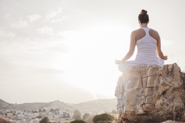 woman meditating on a rock overlook.