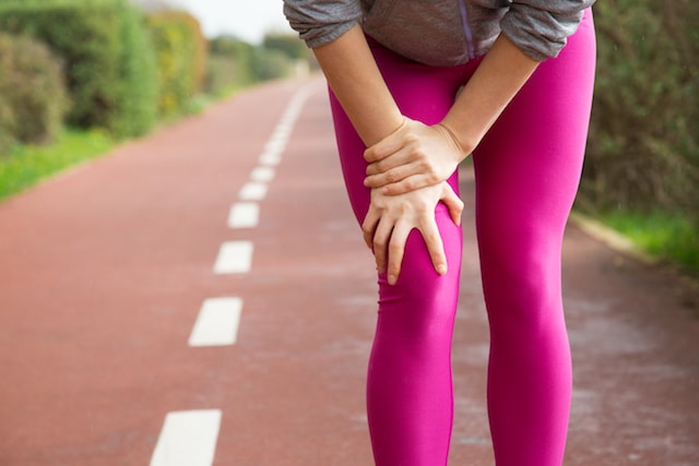 runner in pink tights holding knee quad due to runner's knee.