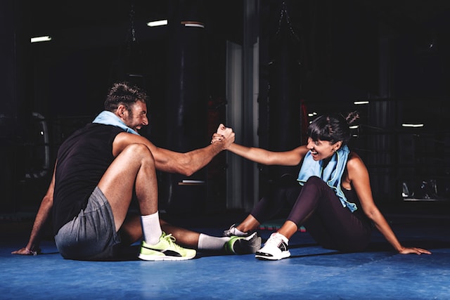 two people at the gym, including a trainer, high-fiving and helping each other up.