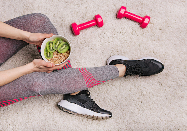 woman sitting on floor with weights and a bowl of food. 