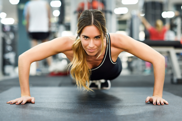 Woman doing a push up in the gym and smiling to the camera.