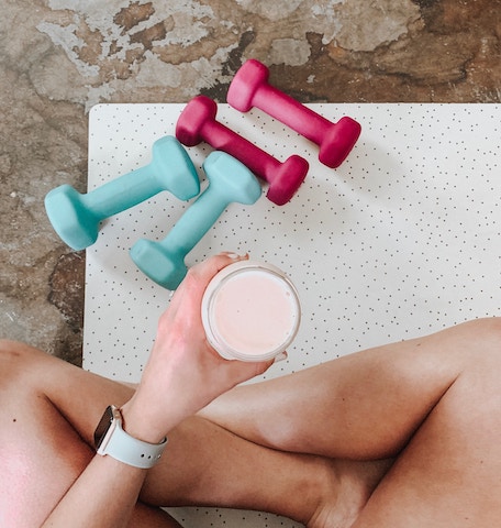 woman siting with weights and a protein shake.