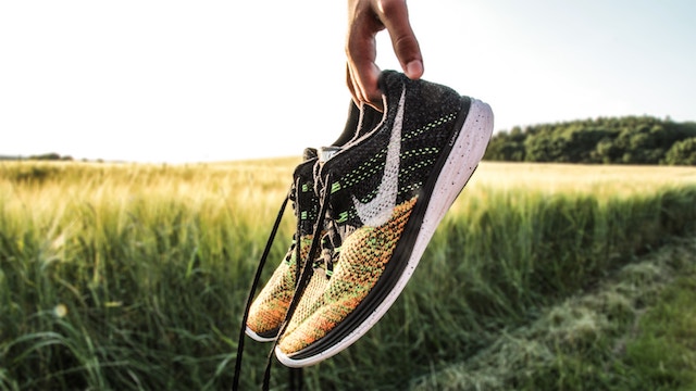 hand holding running shoes in front of a grass field. 