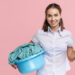 woman holding container of household laundry and a laundry basket of clothes.