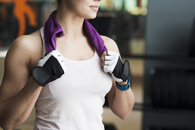 woman looking in distance with  a towel around her neck, she is still in sweaty gym clothes. 