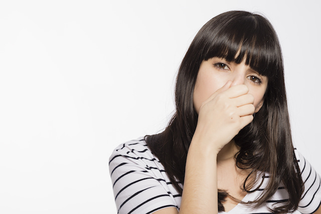 woman covering her nose at the smell of sweaty gym clothes. 